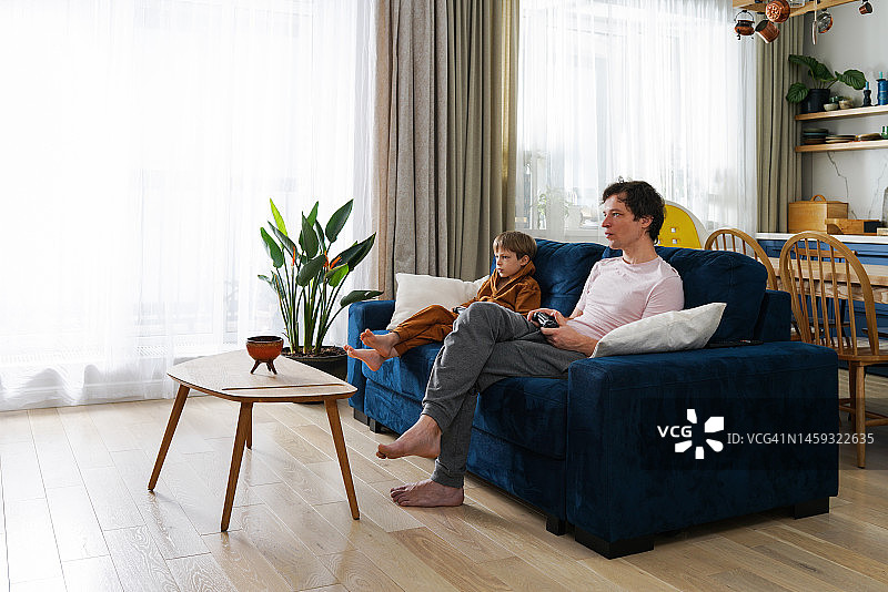 爸爸和儿子一起坐在客厅的蓝色沙发上玩电子游戏图片素材