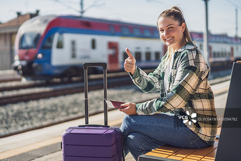 一名女子竖起大拇指，拿着车票坐在火车站的长椅上图片素材