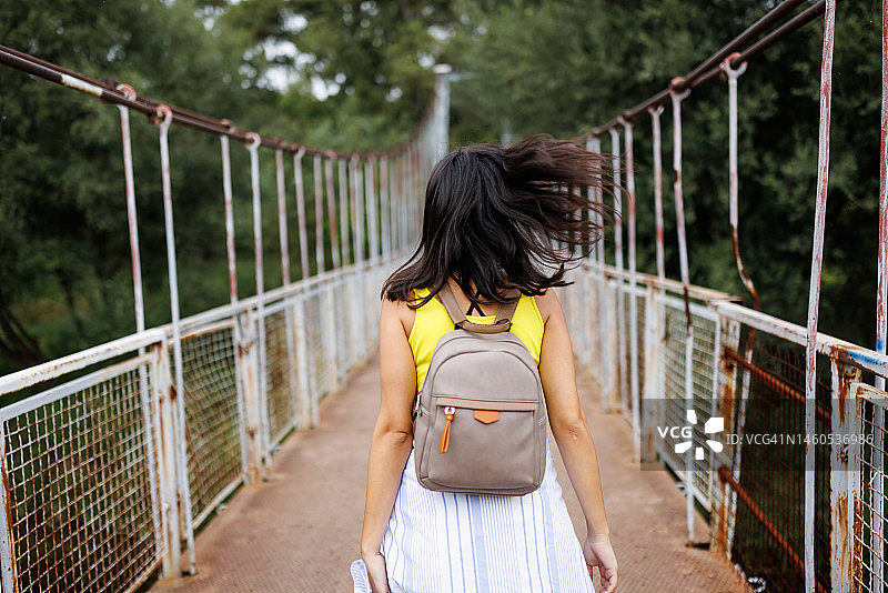 在阳光明媚的日子里，快乐的年轻女子走在大自然的人行桥上图片素材