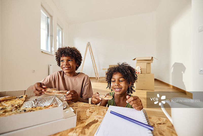 快乐的黑人孩子在新公寓吃披萨。图片素材