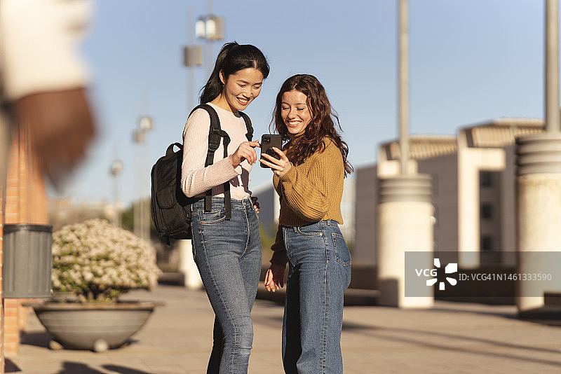 一对年轻的女学生在户外用智能手机聊天图片素材