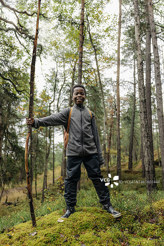假期里，微笑的男孩拿着木棍站在森林里图片素材