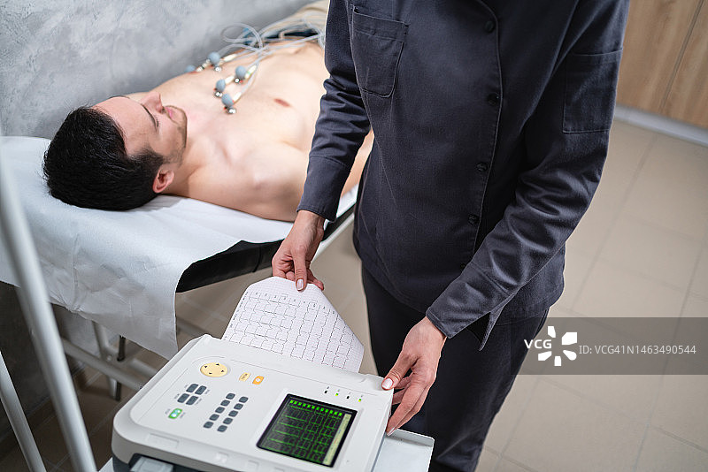 当病人躺在检查台上进行心电图检查时，女护士在分析他的心电图图片素材