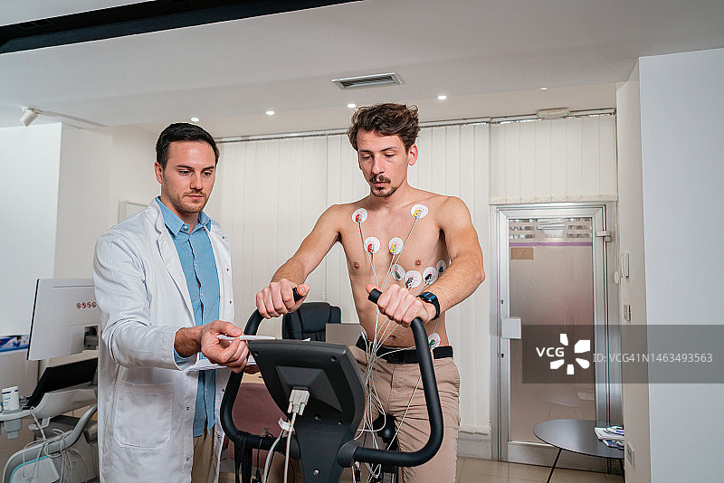 男性病人胸前有电极，在运动自行车上做压力测试，医生观察他图片素材