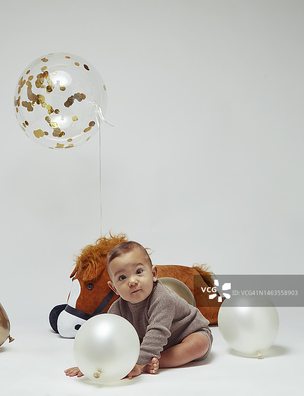 在白色背景下，一个小男孩拿着玩具和飞行的气球在镜头前摆姿势。图片素材