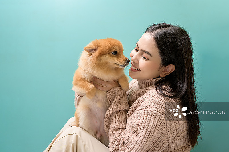 年轻美丽的女子亲吻和拥抱她的狗在绿色背景的肖像。图片素材