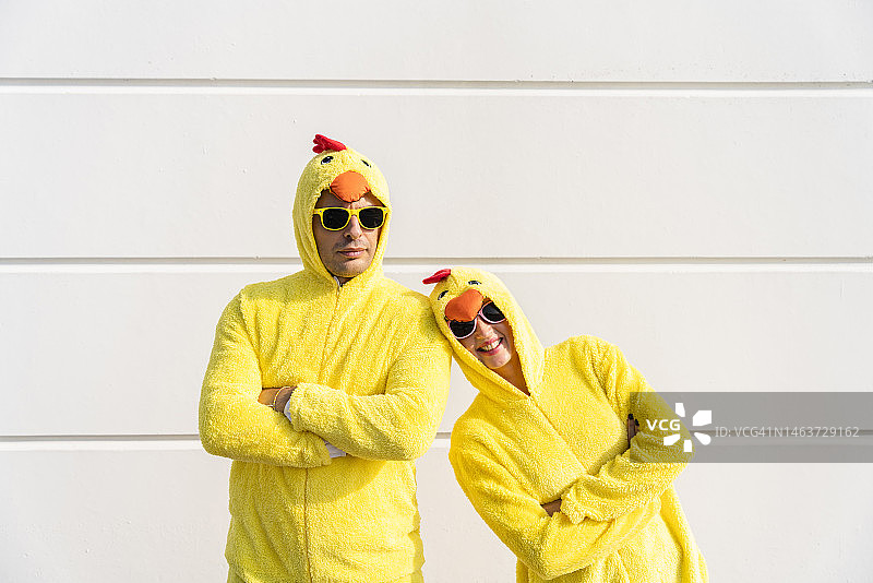 快乐的女人和男人穿着鸡服装，双手交叉站在墙前图片素材