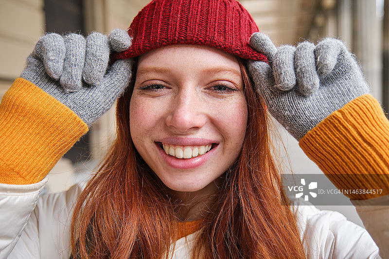 快乐的红发女孩的头像，带着雀斑，戴着红色的帽子和手套图片素材