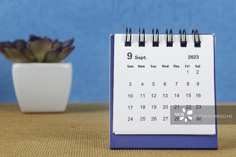 日历桌2023:9月是组织者计划和截止日期的月份，在蓝色纸背景下放置室内植物。图片素材