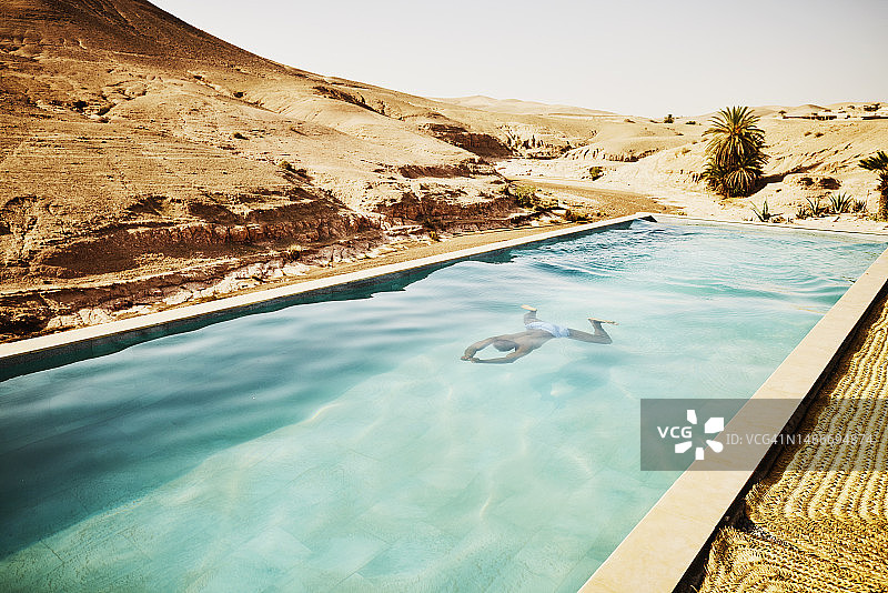 在摩洛哥沙漠营地的游泳池里游泳的男子的宽镜头图片素材