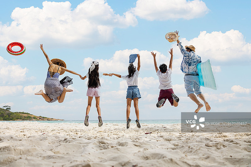 假日，快乐的亚洲家庭一起在海滩上蹦蹦跳跳。一家人手牵着手在海滩上欣赏日落的剪影。快乐家庭旅游度假概念。图片素材