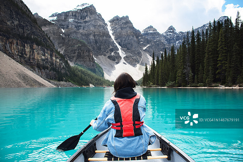 年轻的女孩骑在独木舟上的绿松石湖与山的看法图片素材