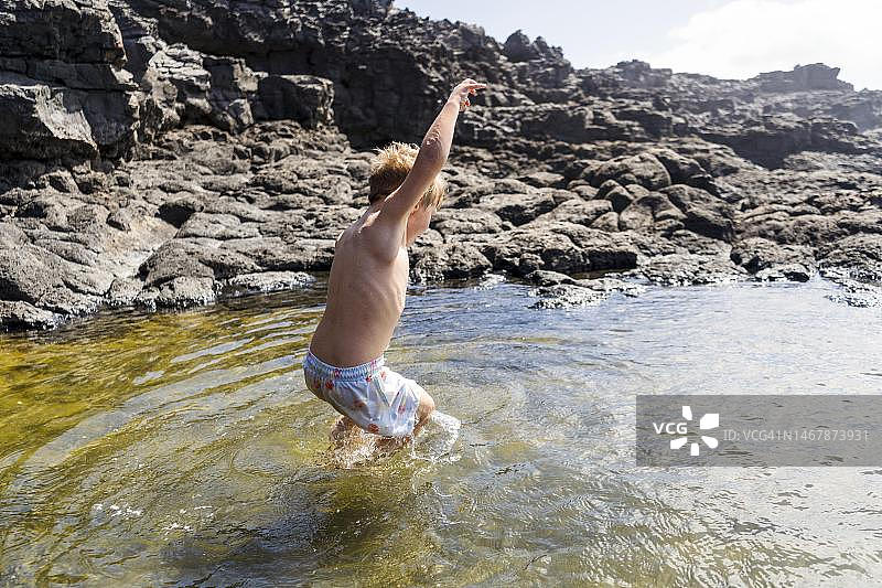 在西班牙加那利群岛的兰萨罗特岛，一个小男孩欢快地在夏康内天然水池中跳跃图片素材
