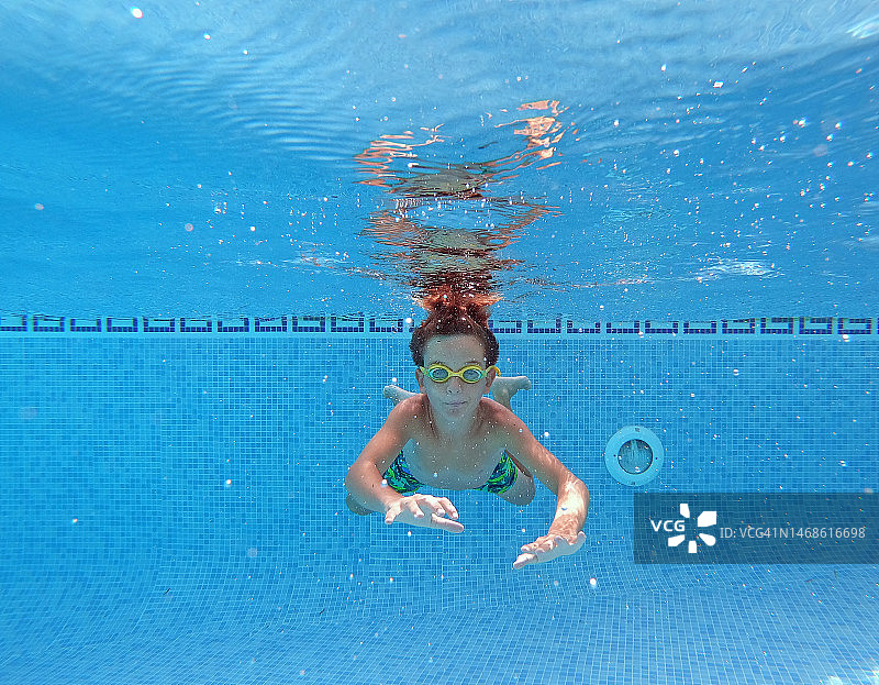 男孩在泳池里享受水下游泳对着镜头。图片素材
