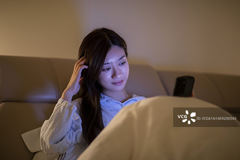 年轻的亚洲女子在卧室使用手机图片素材