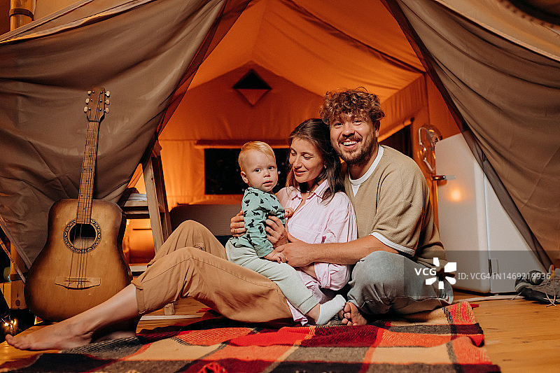 快乐的家庭和可爱的宝宝一起玩耍，在夏天的晚上一起露营。户外休闲休闲的豪华露营帐篷。生活方式的概念图片素材