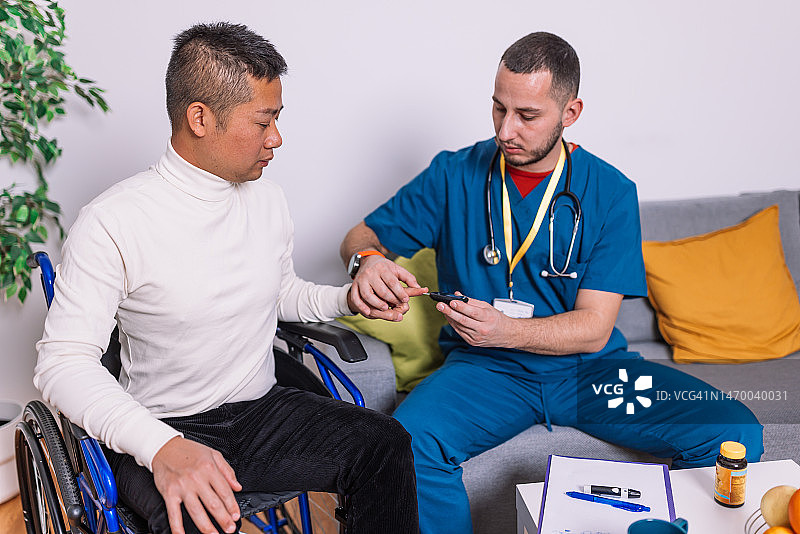一位男护士坐在病人旁边测量他的血糖水平图片素材