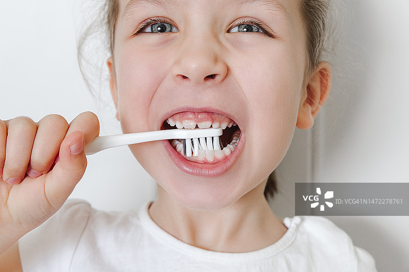 小快乐女孩的肖像用粉红色的牙刷刷牙。白色背景。保健，牙齿健康，个人卫生理念。特写镜头图片素材