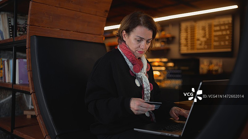 一名女子舒适地坐在咖啡馆里，用她的笔记本电脑和信用卡网购图片素材