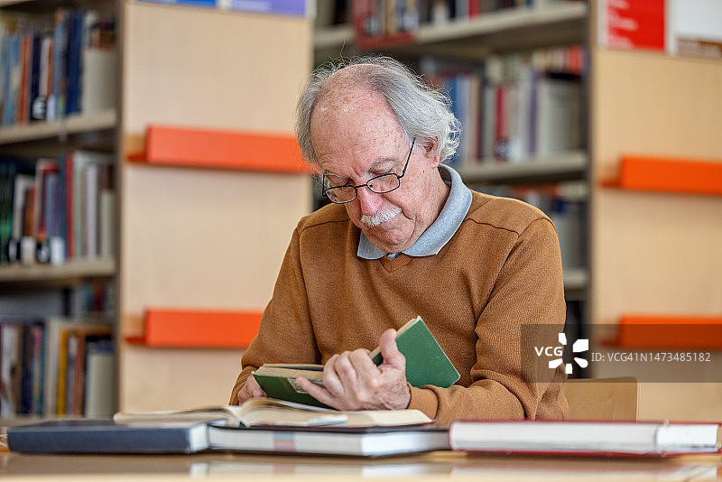 一位年长的白人男子坐在图书馆里看书图片素材