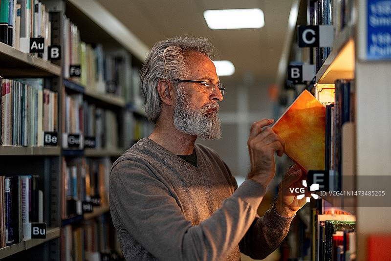 白人退休男子在市图书馆拿起一本书图片素材