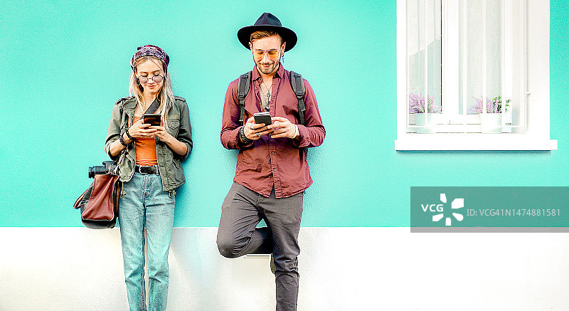 年轻的潮人夫妇在外面的位置用移动智能手机玩得很开心-技术概念与连接的朋友在社交媒体网络上分享故事内容-亮蓝绿色和橙色过滤器图片素材