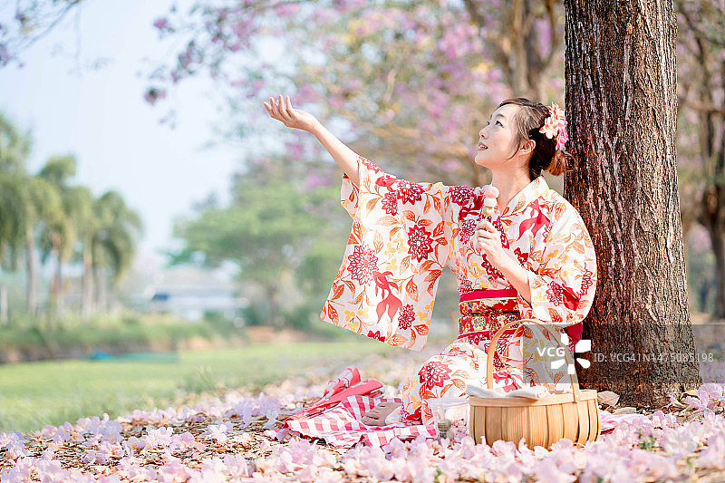 春节。年轻的女士在传统和服坐在和抱在樱花树。图片素材