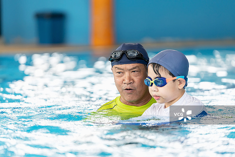 运动使你的身体强壮。在学校的泳池里，资深专业老师教学生游泳，把孩子的头放在水里练习屏住呼吸。周末学习和锻炼。图片素材