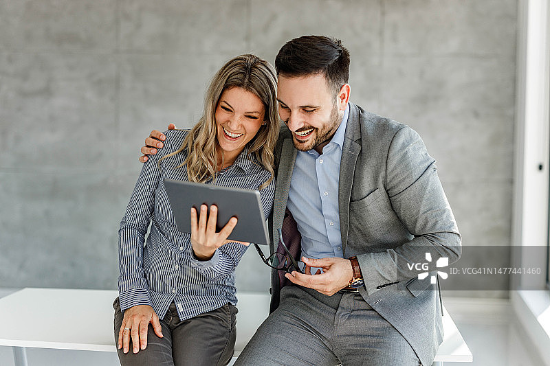 一对幸福的商业情侣在办公室的触摸板上阅读电子邮件。图片素材