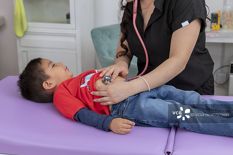一个孩子正在接受他的儿科医生用听诊器检查他的胃图片素材