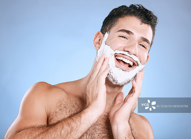 面部，剃须膏涂在胡须上，男人带着微笑，手放在脸上，在工作室模拟中植入产品。豪华剃须泡沫，头发和皮肤护理，快乐男模美容隔离在蓝色背景。图片素材