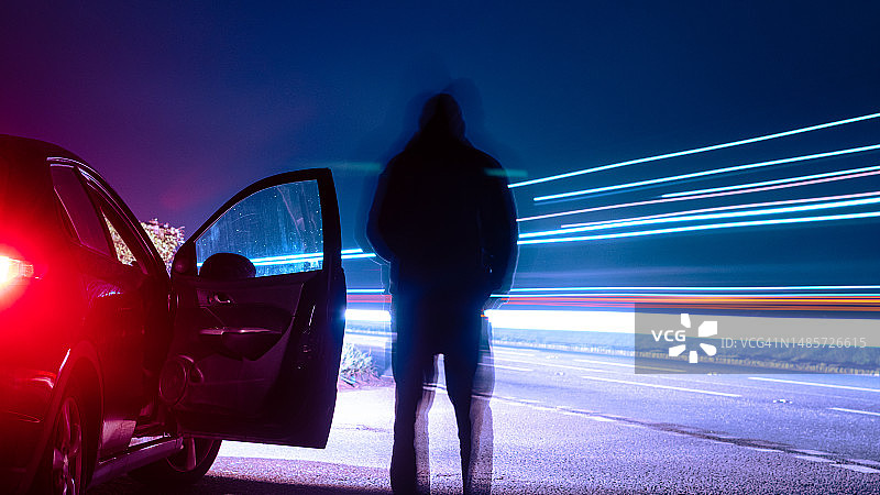 一个模糊的身影，看着交通痕迹。在一个忧郁、雾蒙蒙的夜晚，在一辆车旁边。图片素材