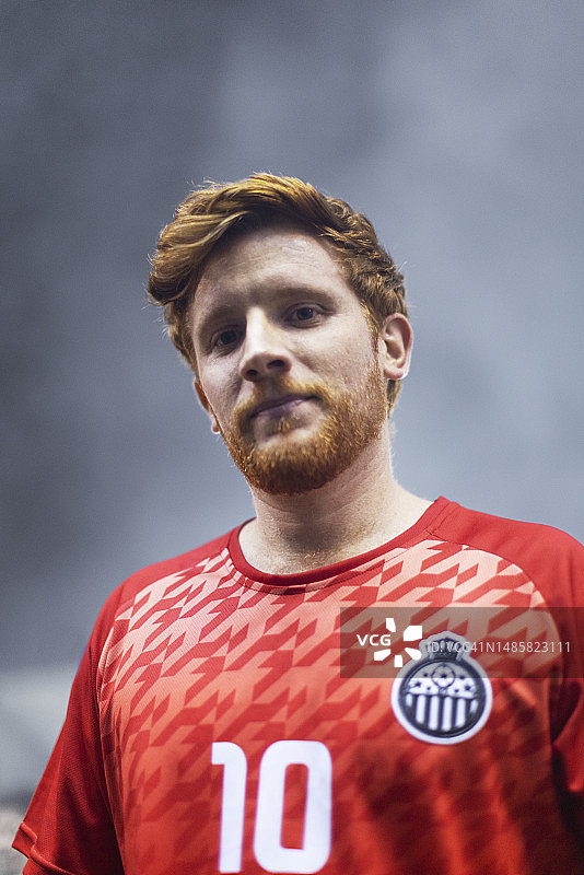 一个红头发的成年男性职业足球运动员看着身后有雾的相机的肖像图片素材