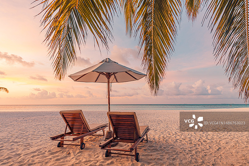 令人惊叹的日落海滩。浪漫的情侣椅子伞。宁静相聚的爱情概念风景，放松的沙滩，美丽的景观设计。度假热带海岛海岸，棕榈叶，田园诗般的海景图片素材