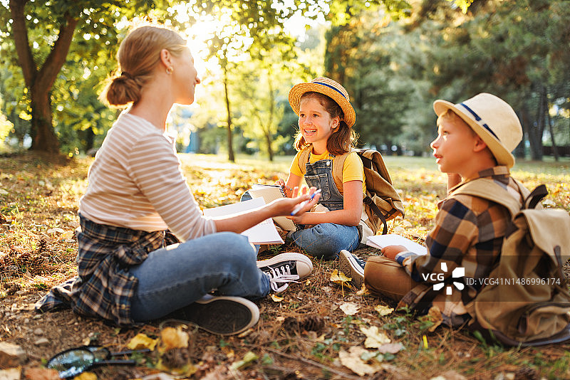 孩子们和微笑的女老师围坐在森林的草地上谈论大自然图片素材
