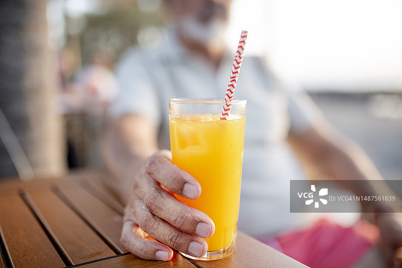 60多岁的外籍现代活跃老人在海滩享受健康的新鲜橙汁图片素材