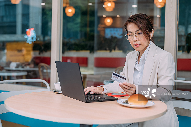 一名亚洲妇女在咖啡店使用手提电脑和信用卡进行网上购物图片素材