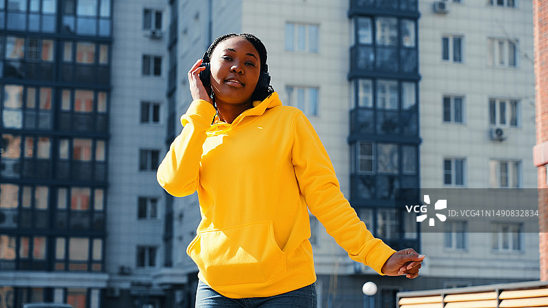 非裔美国妇女在日落时分在城市里用耳机听音乐，跳舞图片素材