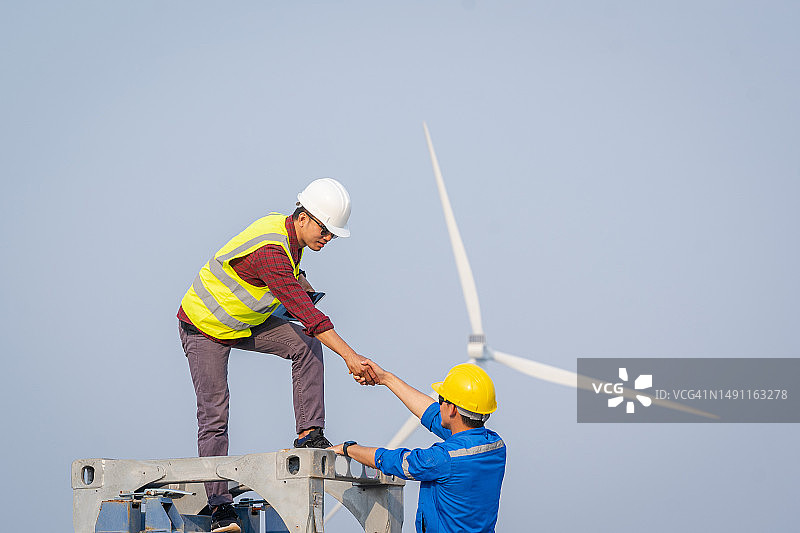 快乐的男性电气工程师和微笑的维修工人在风力涡轮机农场握手。图片素材