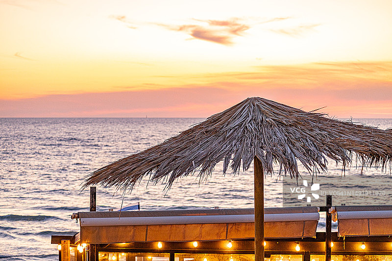 海滩咖啡馆的稻草遮阳伞，映衬着地中海的日落美景图片素材
