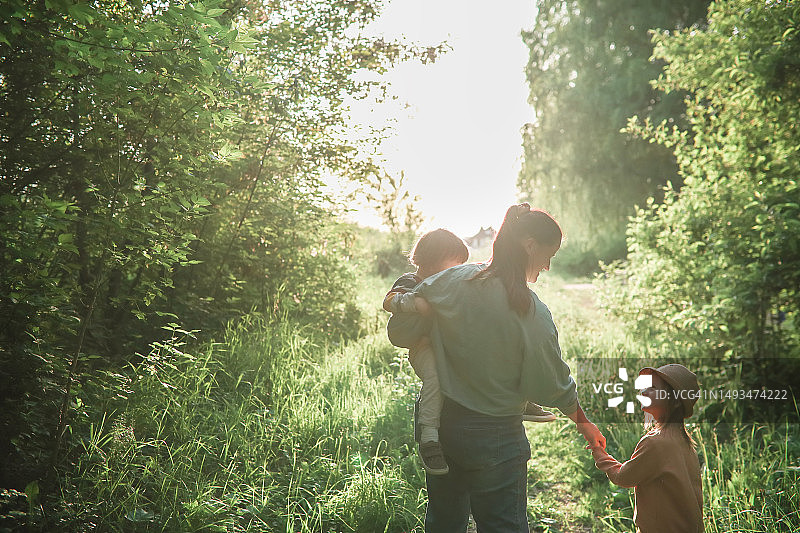 快乐的中年超重妈妈和她的两个孩子因为对大自然的热爱和在森林里徒步旅行而联系在一起。妈妈关心和说话的孩子，背影图片素材