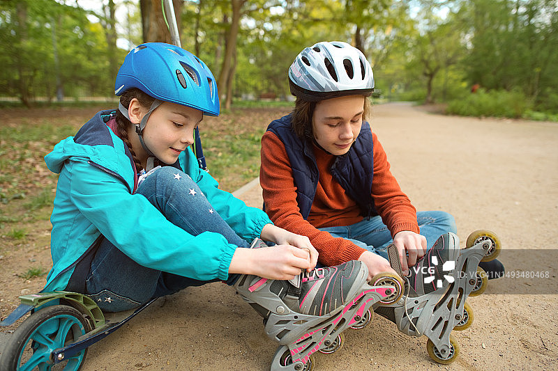 孩子们准备骑车:春天，一个男孩在公园里帮他的妹妹穿上旱冰鞋图片素材