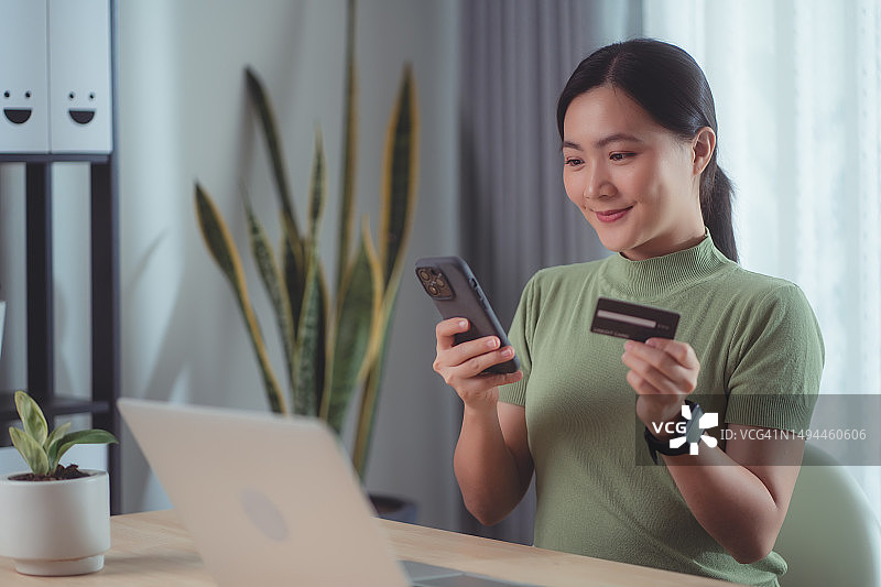 亚洲女性喜欢在家里用信用卡和智能手机进行网上购物。图片素材