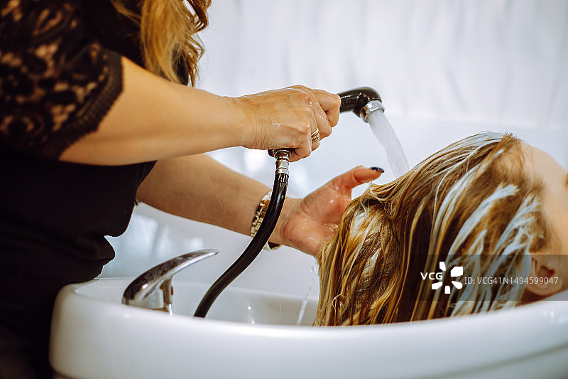 认不出来的女发型师在白色水槽里洗女顾客的金发图片素材
