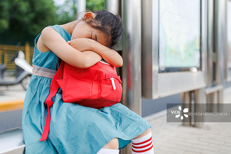 等公共汽车时，累了的小女孩拿着包睡着了图片素材