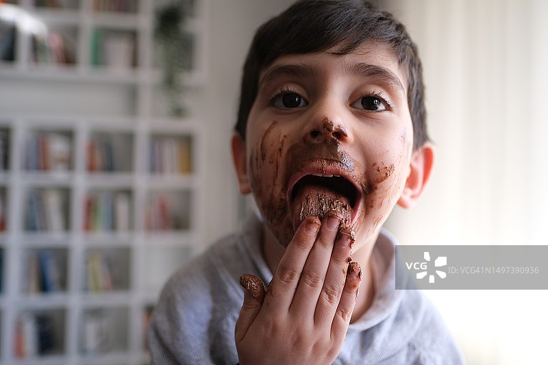 微笑的小男孩舔着脸上的巧克力图片素材
