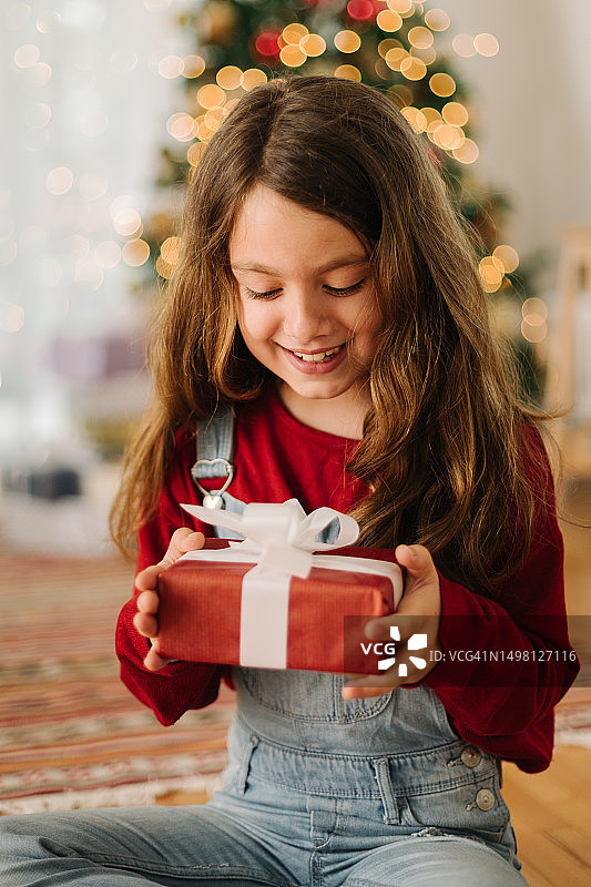 欢快的女孩在圣诞树前拿着圣诞礼物图片素材
