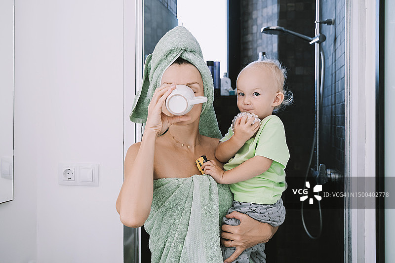 母亲裹着毛巾抱着儿子在浴室外喝咖啡图片素材