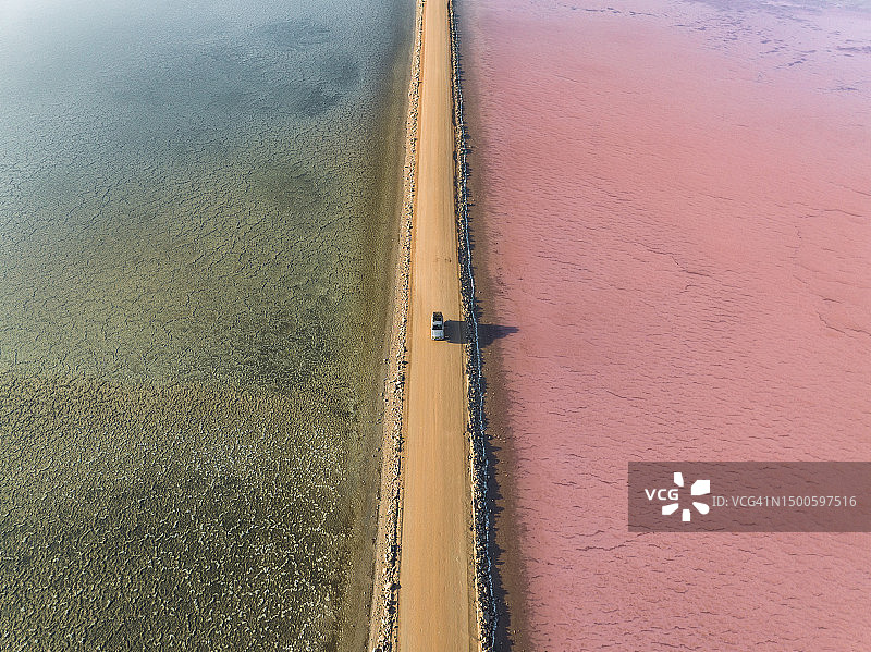 航拍照片显示了一辆4x4在日出时在两个盐湖之间的土路上行驶，澳大利亚南澳大利亚Penong的麦克唐奈湖图片素材