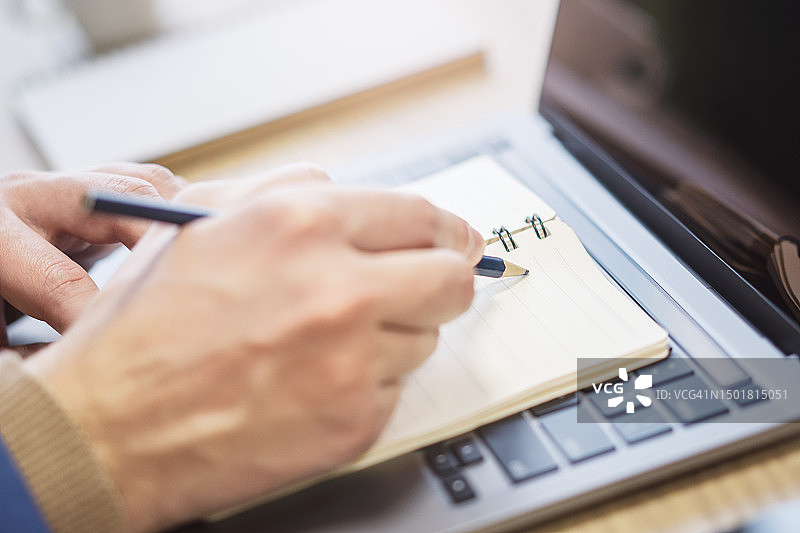 一个男人的手在一个尖端的笔记本电脑上做笔记的近景，周围有一个柔和的模糊图片素材